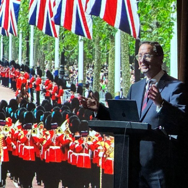 Graham presenting at a lectern with a military parade and Union flags projected behind him